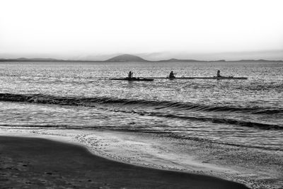 People kayaking in sea against sky