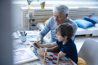 Boy drawing on tablet pc by grandfather in living room