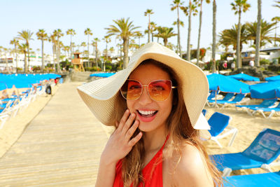 Portrait of cheerful young woman wearing hat at beach