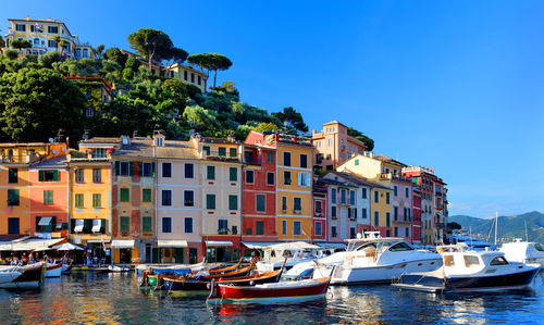 Boats moored in canal by buildings against clear blue sky