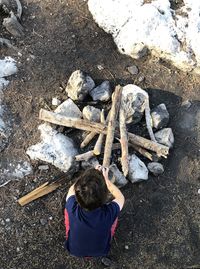 High angle view of boy crouching by rocks and wood on land