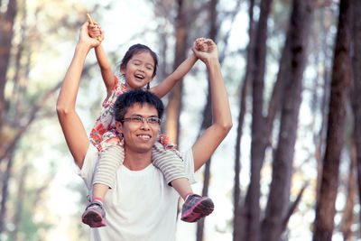 Father carrying daughter on shoulder against trees