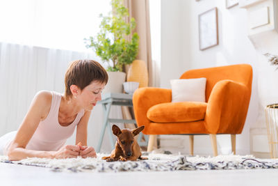 Beautiful adult woman practicing yoga pose with pygmy pinscher dog enjoying