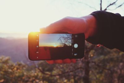 Close-up of hand holding smart phone against sky