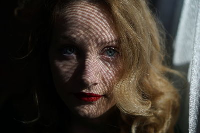 Close-up portrait of beautiful woman by curtain