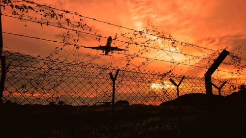 Silhouette of barbed wire on field against sky during sunset
