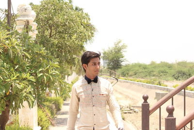 Young man standing by railing against clear sky