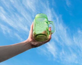Low angle view of hand holding drink against blue sky