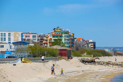 People on beach against buildings in city against clear sky