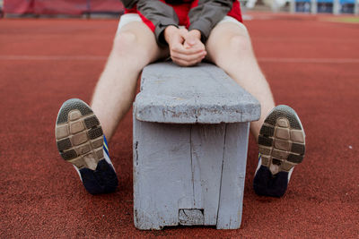 Low section of boy sitting on bench at stadium