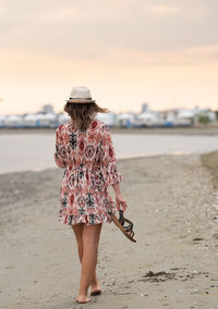 Rear view of woman standing at beach against sky