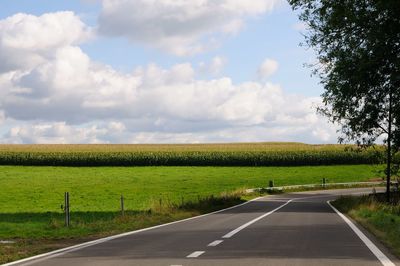 Empty road amidst field against sky