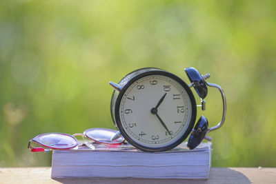 Close-up of alarm clock with eyeglasses and book on table