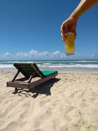 Cropped hand holding drink on beach against sky