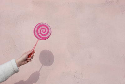 Cropped hand holding lollipop against wall during day