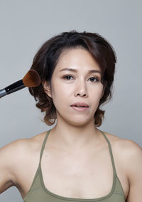 Portrait of beautiful woman applying make-up against gray background
