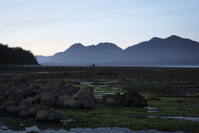 Rocks in sea by mountains against sky