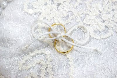 High angle view of gold wedding rings tied up on white lace textile