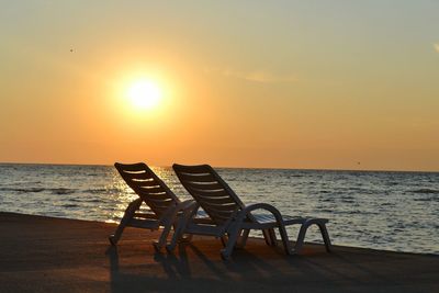 Chairs on beach against sky during sunset