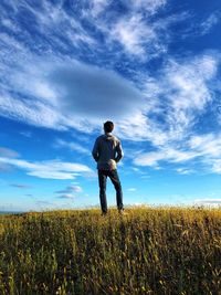 Rear view of man standing on grassy field against blue sky