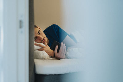 Teenage boy using smart phone while lying on bed at home