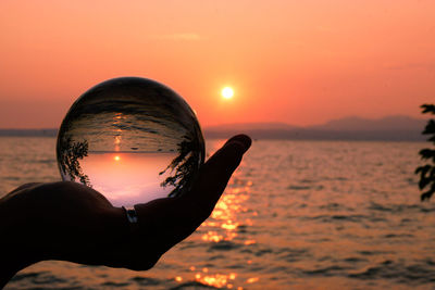 Silhouette hand against sea during sunset