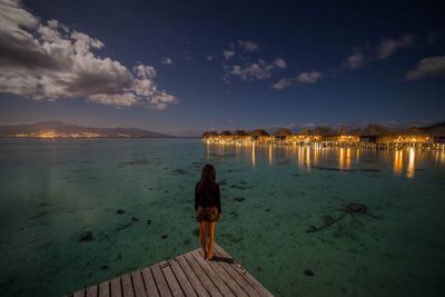 Rear view of woman standing on pier against sky during dusk