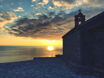 Building by sea against sky during sunset