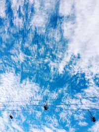 Low angle view of ski lifts against cloudy sky