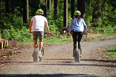 Rear view of people cycling walking on dirt road