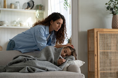 Side view of young woman sitting on bed at home