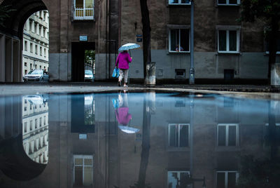Woman walking with umbrella on wet street by buildings during monsoon