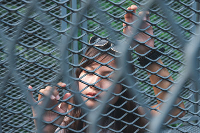 Woman seen through chainlink fence looking away while standing outdoors