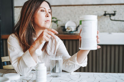 Adult brunette woman having breakfast with dry instant protein vitamin shake in kitchen at home