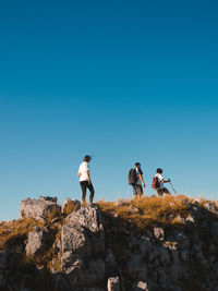 People on rock against clear blue sky