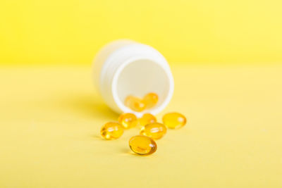 Close-up of pills spilling from bottle against yellow background