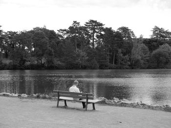 Man sitting on bench by lake against trees