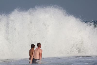 Shirtless friends standing in sea against sky during sunny day