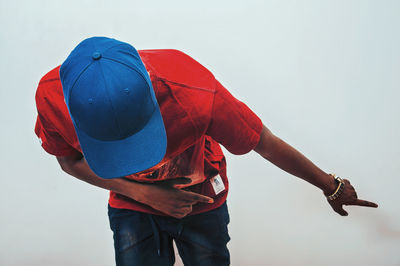 Man in cap pointing while bending against clear sky