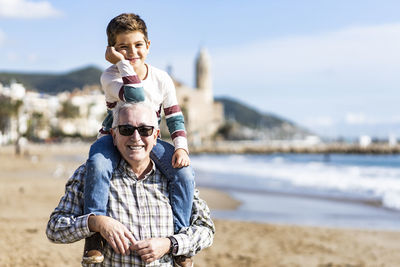 Portrait of happy senior man giving piggyback ride to grandson at beach