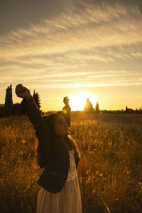 Woman standing on field against sky during sunset