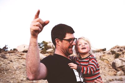 Happy father pointing while carrying son against clear sky