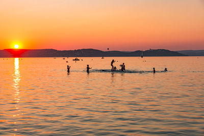 Silhouette people in sea against sky during sunset