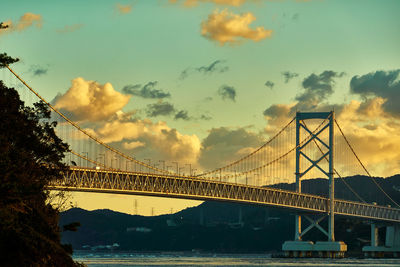 View of suspension bridge against dramatic sky during sunrise