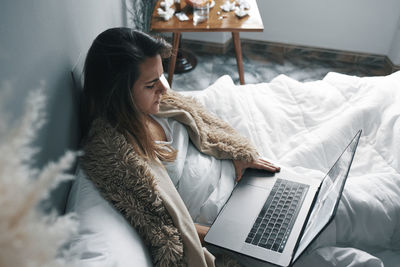 Woman using mobile phone while sitting on bed