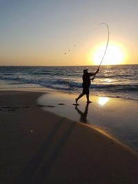 Silhouette mid adult man standing at beach against clear sky during sunset