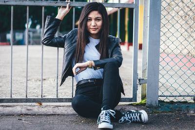 Portrait of smiling young woman sitting against fence