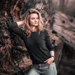 Portrait of young woman standing against tree trunk