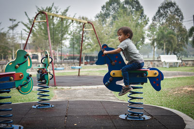 Boy looking away while sitting on rocking horse on playground