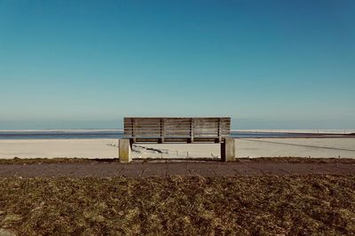 Empty bench on beach against clear sky